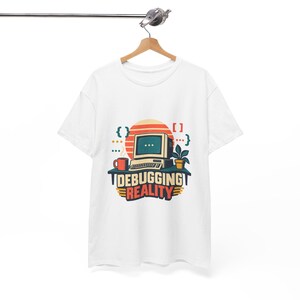 May include: A white t-shirt featuring a graphic of a vintage computer on a desk with a coffee mug and a potted plant. The text reads DEBUGGING REALITY, surrounded by coding brackets and a sunset circle in shades of orange, teal, and yellow.