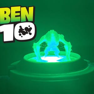 May include: A glowing green figure from Ben 10 is lit from below, standing on a circular base. The Ben 10 logo, in green and white, is in the top left against a green backdrop.