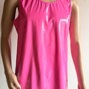 Könnte beinhalten: Ein ärmelloses Tanktop in einem leuchtenden, glänzenden Pink. Das Kleidungsstück verfügt über einen Rundhalsausschnitt und eine glatte, reflektierende Oberfläche, die das Licht einfängt und einen deutlichen Glanz auf der Vorderseite erzeugt.