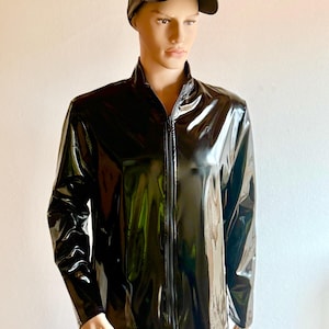 Könnte beinhalten: Eine schwarze, hochglänzende Vinyljacke mit durchgehendem Frontreißverschluss und eine passende schwarze Vinyl-Baseballkappe. Die Jacke verfügt über einen Stehkragen und lange Ärmel mit einer glatten, reflektierenden Oberfläche.