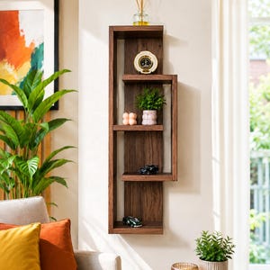 May include: A vertical wall-mounted wooden shelf unit with a dark brown finish, featuring an asymmetrical design with four distinct display levels. The shelves hold a glass diffuser, a round gold-rimmed clock, a green plant, and small toy cars.