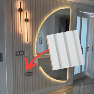 May include: A white rectangular wall panel featuring three vertical grooves and a smooth finish. The panel is shown against a background of a wall with matching vertical slats, a large semi-circular mirror with backlighting, and two wall lamps.