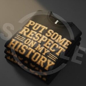 May include: A stack of black sweatshirts with the text "PUT SOME RESPECT ON MY HISTORY" in gold lettering. The sweatshirts are folded neatly, with the text prominently displayed on the top shirt.
