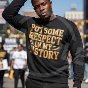 May include: Black sweatshirt with the text "PUT SOME RESPECT ON MY STORY" in gold and white lettering. The sweatshirt is a crew neck style. The person in the image is wearing the sweatshirt.