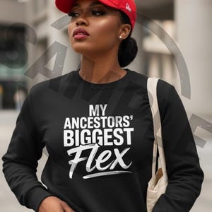 May include: Black sweatshirt with the text "MY ANCESTORS' BIGGEST Flex" in white. A red baseball cap with a white logo is worn on the head. The sweatshirt is a crew neck style.