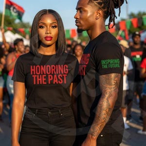 Op de afbeelding: Twee mensen dragen zwarte t-shirts met tekst. Het shirt van de vrouw zegt "HONORING THE PAST" in het rood. Het shirt van de man zegt "INSPIRING THE FUTURE" in het groen. Beide dragen een zwarte broek. Mensen en vlaggen zijn op de achtergrond.