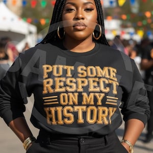 May include: Black sweatshirt with gold lettering that reads "PUT SOME RESPECT ON MY HISTORY". The sweatshirt is paired with black pants. The person is wearing gold hoop earrings and a gold bracelet.