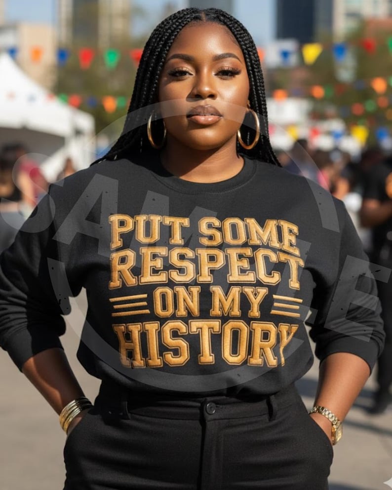 May include: Black sweatshirt with gold lettering that reads "PUT SOME RESPECT ON MY HISTORY". The sweatshirt is paired with black pants. The person is wearing gold hoop earrings and a gold bracelet.