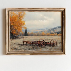 Puede incluir: Pintura de paisaje enmarcada que representa una escena rural con un carro rojo en un campo. La obra presenta un marco dorado, un cielo nublado y árboles con follaje naranja. La pintura evoca un ambiente otoñal.