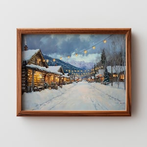 May include: A framed winter landscape painting depicts a snow-covered village street lined with wooden buildings. String lights illuminate the street and buildings. Mountains are visible in the background under a cloudy sky. The painting is in a brown wooden frame.