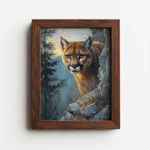 Op de afbeelding: Een ingelijste afbeelding van een poema die achter een rotsformatie vandaan kijkt. De poema heeft goudbruine vacht en doordringende ogen. De achtergrond toont een bos in blauwe en groene tinten. De lijst is donkerbruin.