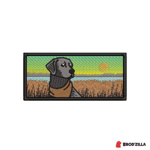 Può includere: Toppa ricamata raffigurante un cane Labrador Retriever nero in un campo con un tramonto. Il cane indossa un collare marrone. La toppa ha un bordo nero. Il testo "BROD'ZILLA" è nell'angolo in basso a destra.