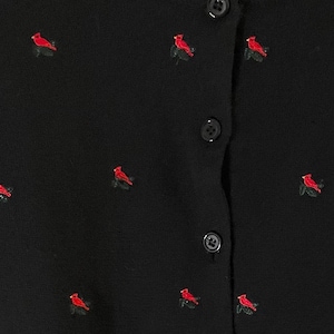 May include: Black cardigan with red cardinal bird embroidery. The button-up sweater features small, embroidered cardinals dotted across the fabric. The cardinals are red with green detailing.