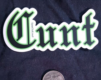 May include: A white sticker with the word "CUNT" in a black gothic font, outlined in green. The sticker also has the text "SpazOutLoud" in a smaller font. A U.S. quarter is next to the sticker.