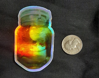 May include: A holographic sticker of a glass jar with a colorful, abstract design. The jar is filled with a swirling, iridescent liquid.