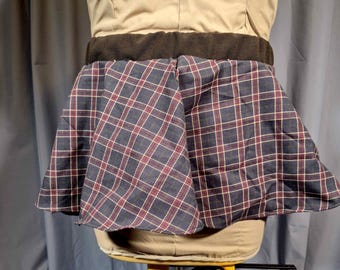 May include: A plaid skirt in navy blue, red, and white, displayed on a mannequin. The skirt has a flared shape and a dark brown waistband. The mannequin is wearing a tan top.