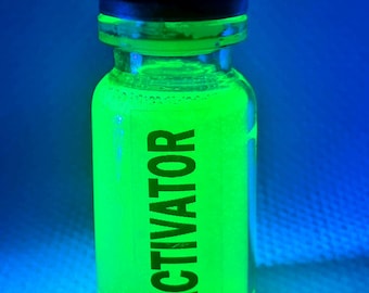 May include: A clear glass bottle with a black cap and a green liquid inside. The bottle is labeled "ACTIVATOR".