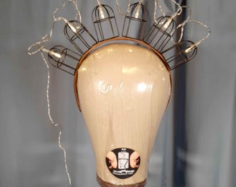 May include: A brown headband with a wire frame and small light bulbs. The headband is on a mannequin head. The lights are connected to a battery pack.