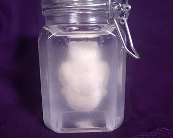 May include: A clear glass jar with a metal clasp lid, containing a white, opaque, round object submerged in clear liquid.