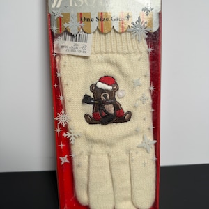 May include: Cream-colored knit glove with a Christmas teddy bear design. The bear wears a red Santa hat and scarf. The glove is in a clear plastic box with the text "ISO" and "One Size Glove".