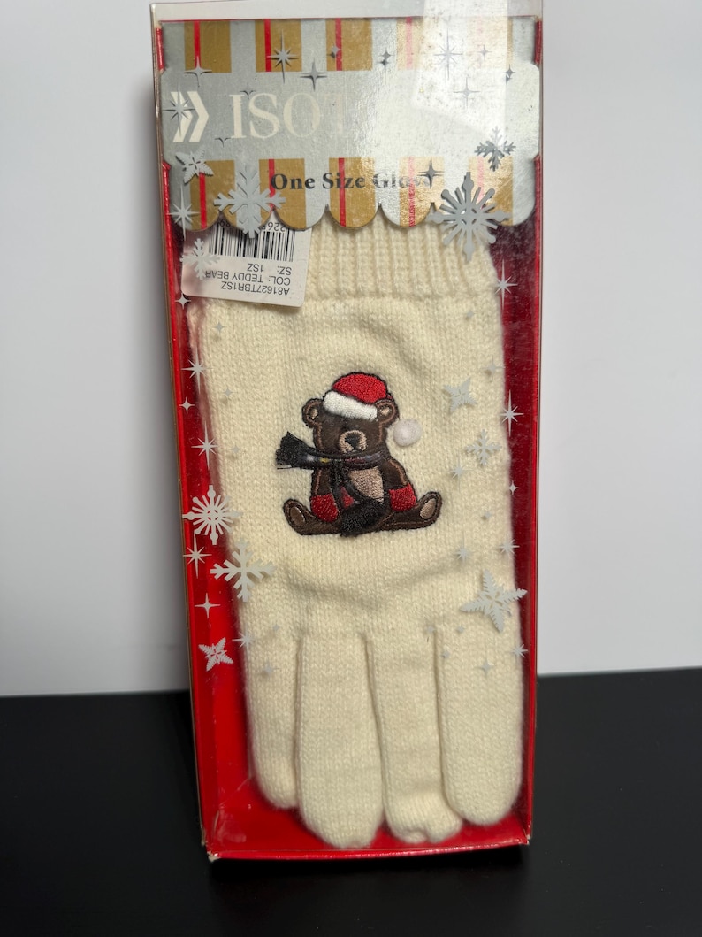May include: Cream-colored knit glove with a Christmas teddy bear design. The bear wears a red Santa hat and scarf. The glove is in a clear plastic box with the text "ISO" and "One Size Glove".