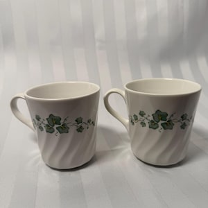 Può includere: Una tazza di ceramica bianca con manico nero e la scritta "But First, Coffee" in grassetto nero. La tazza è posta su uno sfondo sfocato, che suggerisce un'atmosfera accogliente.
