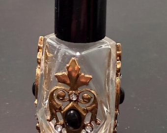 装飾が施されたミニチュアのヴィンテージ香水瓶。透明なガラスに金と黒の装飾が施されています。