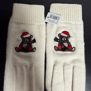May include: A pair of ivory-colored knit gloves. Each glove features an embroidered teddy bear wearing a red Santa hat, a black scarf, and red boots. The gloves have a ribbed cuff and are designed for winter wear.