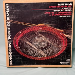May include: A vintage Ruby Band relish plate in its original box. The red glass plate has three compartments and a 12-inch diameter. The box features text in English and French, including "Diamond Point" and "Indiana Glass."