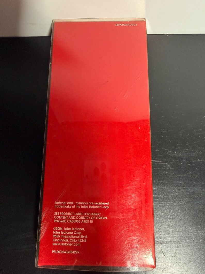 May include: A rectangular package with a bright red surface. The package has text in white, including the Isotoner trademark and company information. The package is sealed in clear plastic.