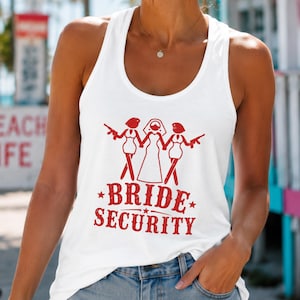 Puede incluir: Una camiseta de tirantes blanca con espalda nadadora que presenta un estampado gráfico rojo de tres figuras, la central con velo de novia y las dos laterales sosteniendo armas de fuego, junto al texto rojo BRIDE SECURITY con estrellas.