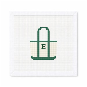 May include: A cross-stitch design of a tote bag with a green outline and handle, and a cream-colored body. The letter "E" is stitched in green on the front of the bag. The design is set against a white background.