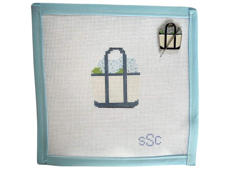 May include: Needlepoint canvas with a light blue border. The canvas features a stitched design of a tote bag with a light blue handle and a small pin of a tote bag with a needle. The initials "sSc" are stitched in the bottom right corner.