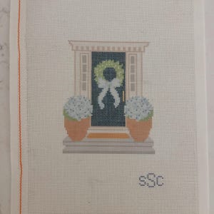 May include: Needlepoint canvas featuring a front door scene. The door is dark blue with a green wreath and white bow. Two potted blue hydrangeas flank the door. The canvas has an orange border on the left side and the initials "sSc" in the lower right corner.