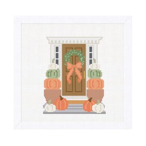 Op de afbeelding: Een kruissteekontwerp van een voordeur versierd voor de herfst. De bruine deur heeft een groene krans en een oranje strik. Stapels pompoenen in oranje, groen en wit flankeren de deur, wat een herfstige sc&egrave;ne cre&euml;ert.