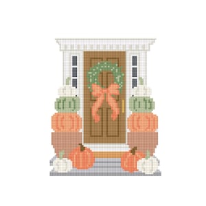 Op de afbeelding: Een kruissteekontwerp van een voordeur versierd voor de herfst. De bruine deur heeft een groene krans met een perzikkleurige strik. Stapels pompoenen in oranje, groen en wit flankeren de deur.