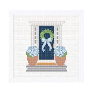 May include: A cross-stitch image of a navy blue front door with a green wreath and a light blue bow. Two potted blue hydrangeas flank the door. The door is framed by white trim and a white background.