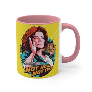 May include: A white ceramic mug with a pink rim and handle. The mug features a yellow background with a colorful illustration of a woman with red hair and a tiger. The text on the mug reads "I will not be lectured about sexism and misogyny by this man. Not now. Not ever!"