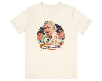 Puede incluir: Una camiseta blanca con un gráfico de un hombre siendo arrestado por dos policías. El gráfico está en un círculo con el texto "What is the Chinese eating a meal? A succulent Chinese meal?" impreso debajo del círculo.