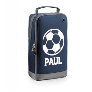 May include: A navy blue football boot bag featuring a white football graphic and the name "PAUL". The bag has grey trim, a handle, and a zip closure. Dimensions are approximately 30cm high.