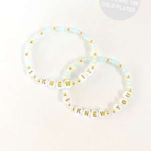 May include: Two stretch bracelets featuring light blue and white beads, small gold-tone beads, and white letter beads with gold text. One bracelet spells I KNEW IT and the other spells I KNEW YOU. Text on image: ALL GOLD BEADS ARE 18K GOLD PLATED.