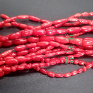 Pode incluir: Três fios de contas de coral vermelho, cada fio com um tamanho de contas diferente. As contas são de forma oval e têm um acabamento liso e polido.