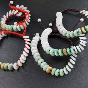 May include: Four jade bracelets with red and brown string closures. The bracelets are made of round, flat jade beads with a green and white colour pattern.