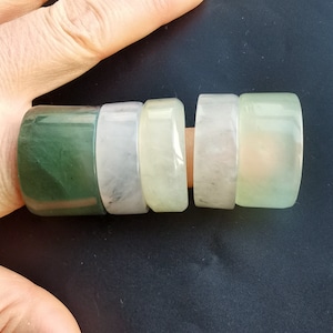 May include: Five jade rings stacked on a finger. The rings are different sizes and shades of green and white.