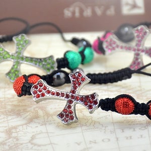 Puede incluir: Cuatro pulseras con cordón negro y cuentas rojas, verdes y rosas. Cada pulsera presenta un dije de cruz plateada con brillantes de colores.
