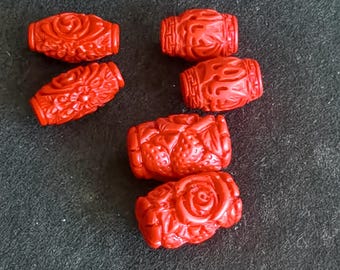Può includere: Sei perline rosse scolpite con intricati disegni floreali e geometrici. Le perline di forma ovale sembrano essere realizzate in un materiale solido. Lo sfondo è grigio scuro. Adatto per la creazione di gioielli.
