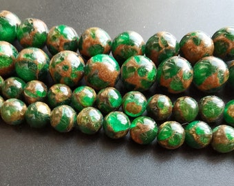 Puede incluir: Una hebra de cuentas ovaladas de color verde y dorado. Las cuentas están hechas de vidrio y tienen un patrón moteado.