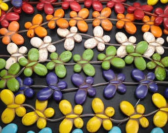 Könnte beinhalten: Eine Reihe bunter Schmetterlingsperlen aus Türkis, Blau, Gelb, Grün, Lila, Weiß, Orange und Rot. Die Perlen sind auf einer durchsichtigen Gummikordel aufgefädelt.