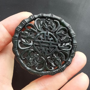 May include: A round, black jade pendant with intricate carvings of a Chinese knot and floral designs. The pendant is carved with a delicate openwork design.