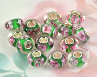 May include: A collection of green and pink glass beads with floral designs. The beads have a silver metal core and are designed for jewellery making.